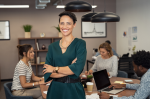 Female blue collar worker smiling at the camera while colleagues are working on the background.